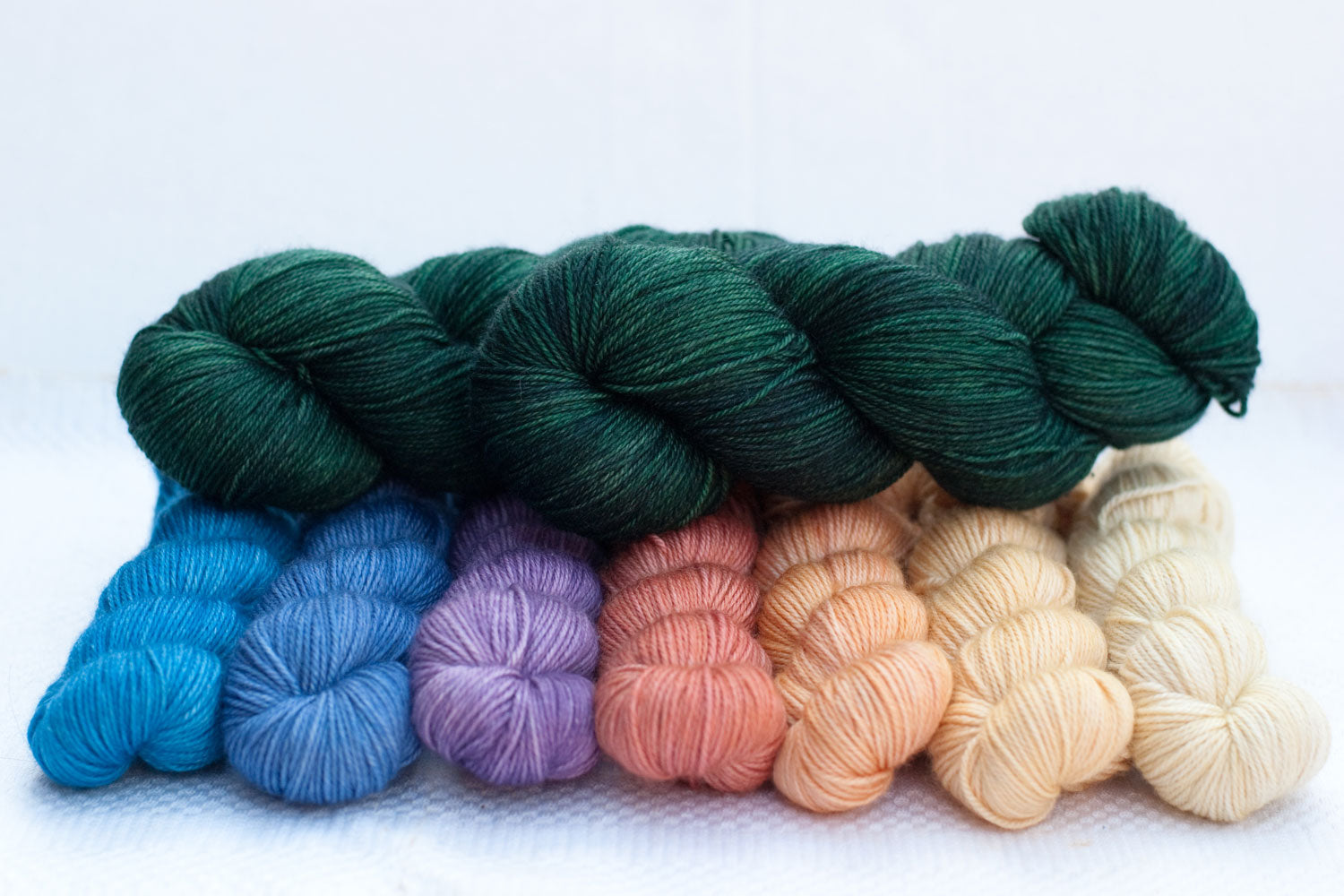 two full skeins of dark green yarn arrange on top of 7 gradient mini-skeins