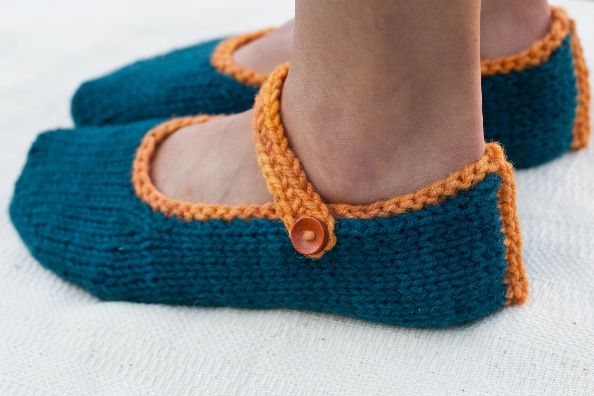 left side of woman's feet in hand-knit slippers showing button and strap detail