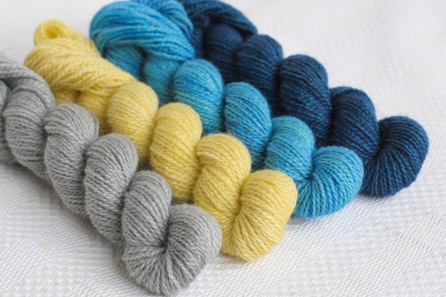 Set of four hand-dyed mini-skeins in pale grey, yellow, light blue, and dark blue