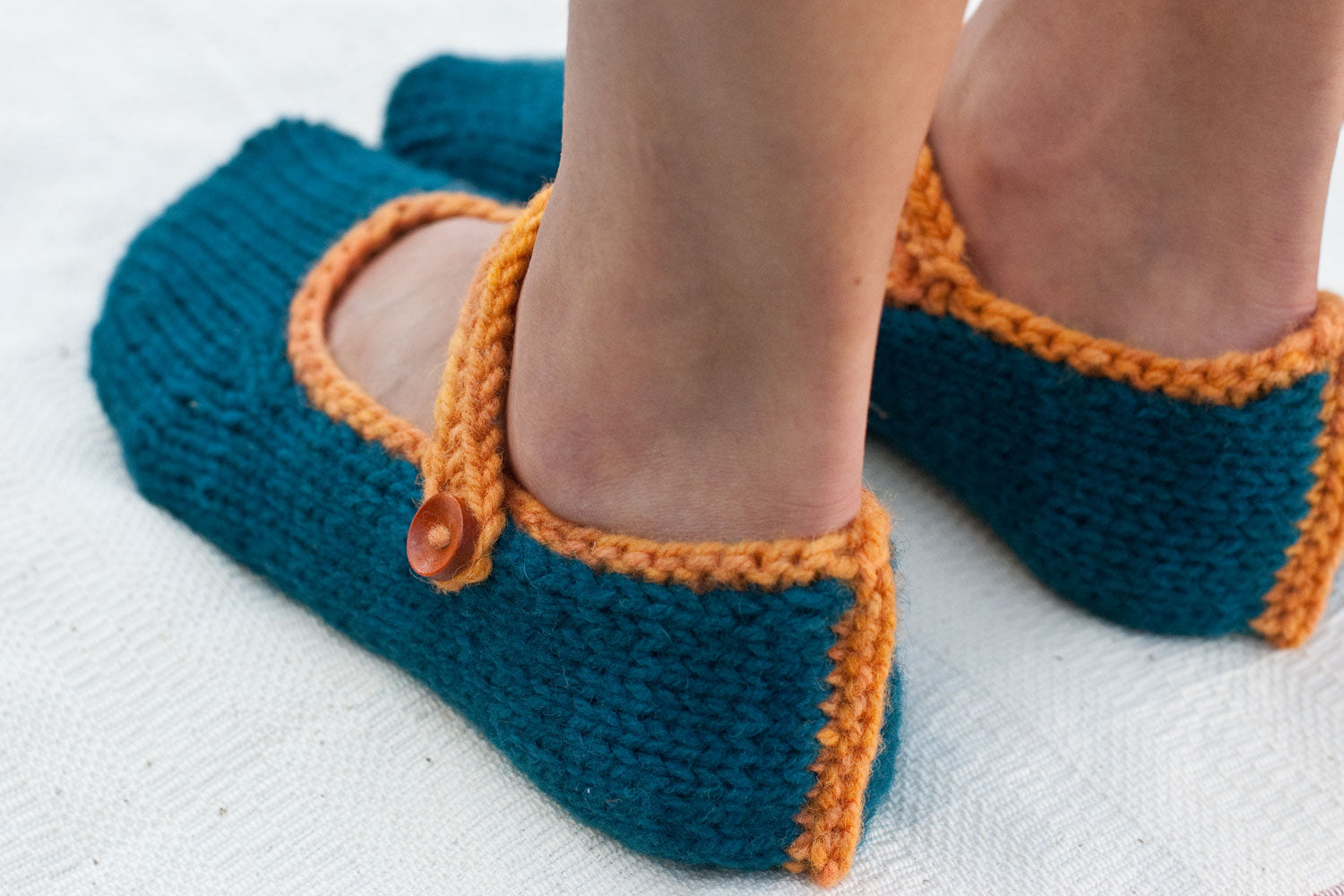 woman's feet wearing hand-knit slippers with sporty trim, ankle straps, and buttons