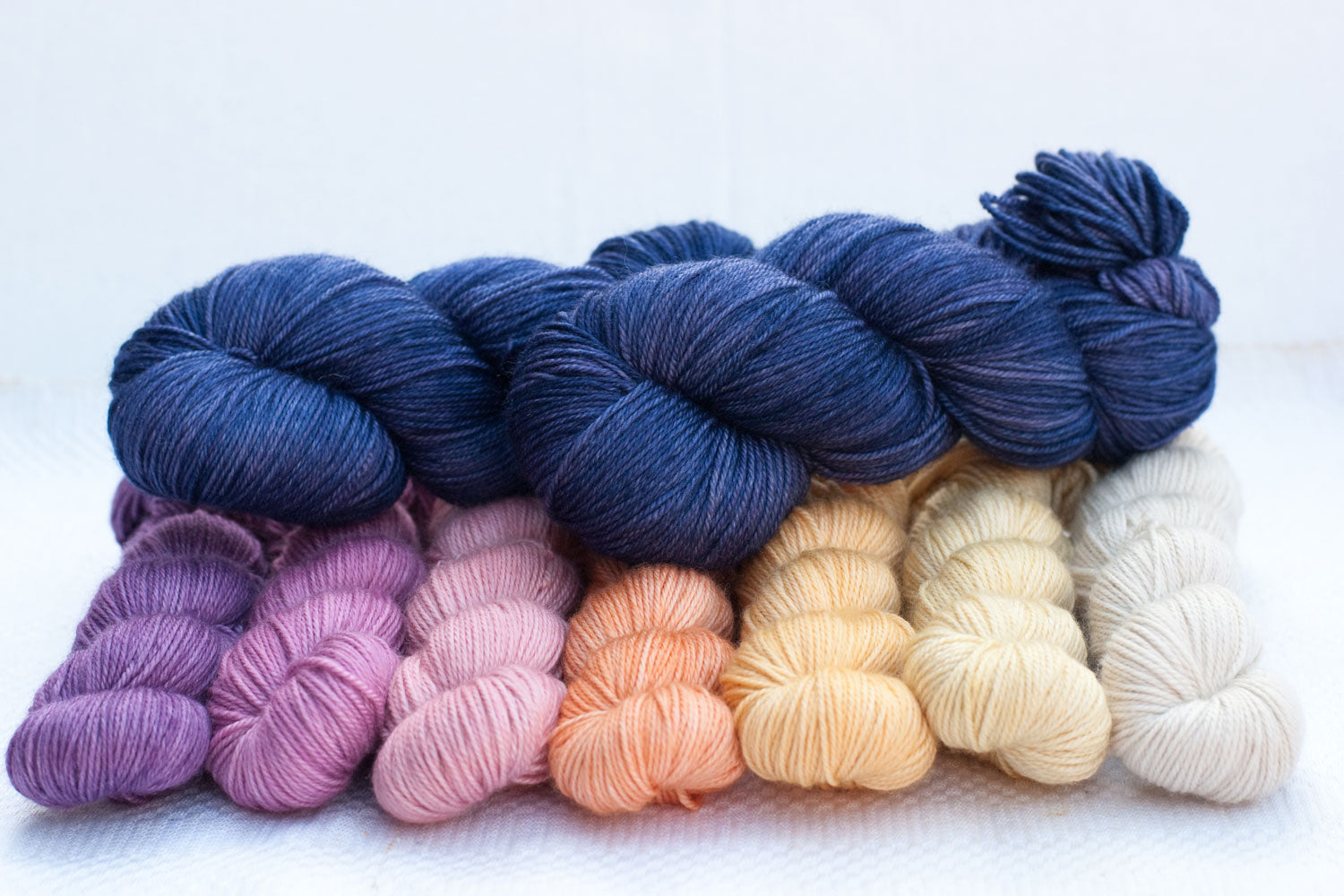 2 full skeins of dark purple yarn contrasted with a purple, pink, peach and cream gradient set