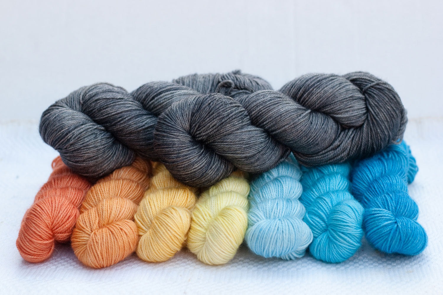 2 full skeins of medium grey yarn contrasted with gradient set of oranges, yellows, and blues
