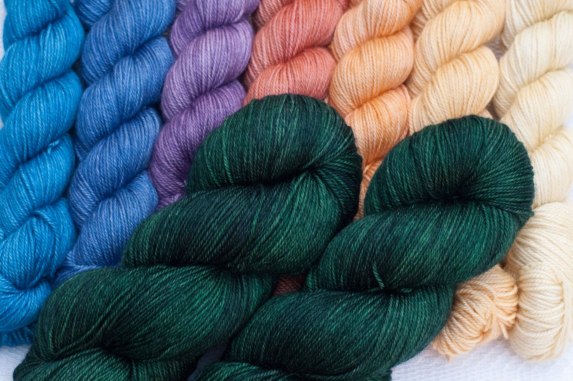 mountain musings mkal hand-dyed yarn set: dark green main colour with blue, purple, salmon, peach and cream gradient set