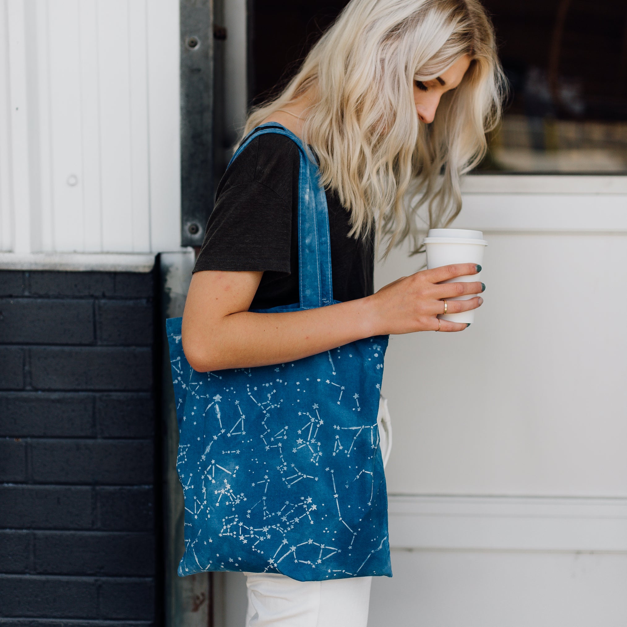 Woman carrying take-out coffee and wearing shoulder bag dyed using clay resist and a stencil to create constellation patterns